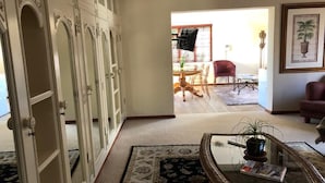 A spacious living room with a large open door leading to a dining area. There is a glass coffee table with a plant, a red chair, and a framed picture on the wall. - Cape Grandeur (Cape Town)