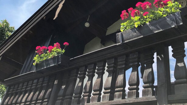 Ein Gebäude mit einem Balkon, der Holzgeländer und Blumenkästen mit rosa Blüten besitzt.