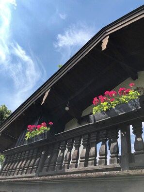 A building with a balcony featuring wooden railings and flower boxes with pink flowers.