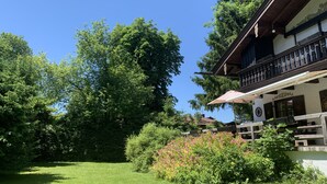 Ein traditionelles Chalet mit Balkon, umgeben von üppiger Vegetation und einem gepflegten Rasen.