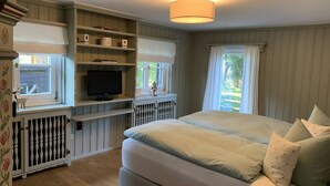 Ein Schlafzimmer mit einem großen Bett, einem Fernseher in einer eingebauten Schrankwand und einem Fenster mit Vorhängen.