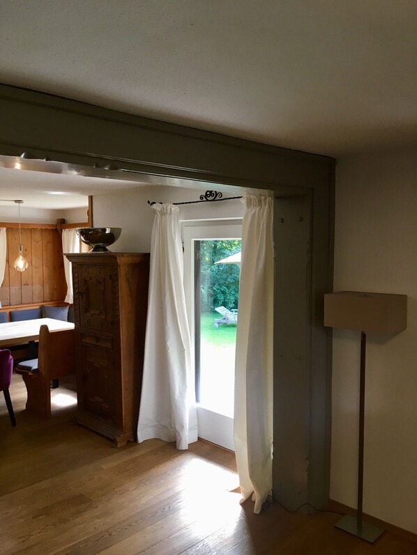 A room with wooden flooring, a dining table with chairs, a wooden cabinet, a floor lamp, and a window with curtains.