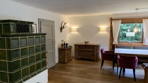 Ein Zimmer mit einem Holzkasten, einem Tisch mit Stühlen, einem Kamin und einem Fenster mit Vorhängen.