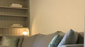 Ein modernes Wohnzimmer mit einem grauen Sofa, mehreren Kissen, einem Holztisch und einem Bücherregal mit Büchern.
