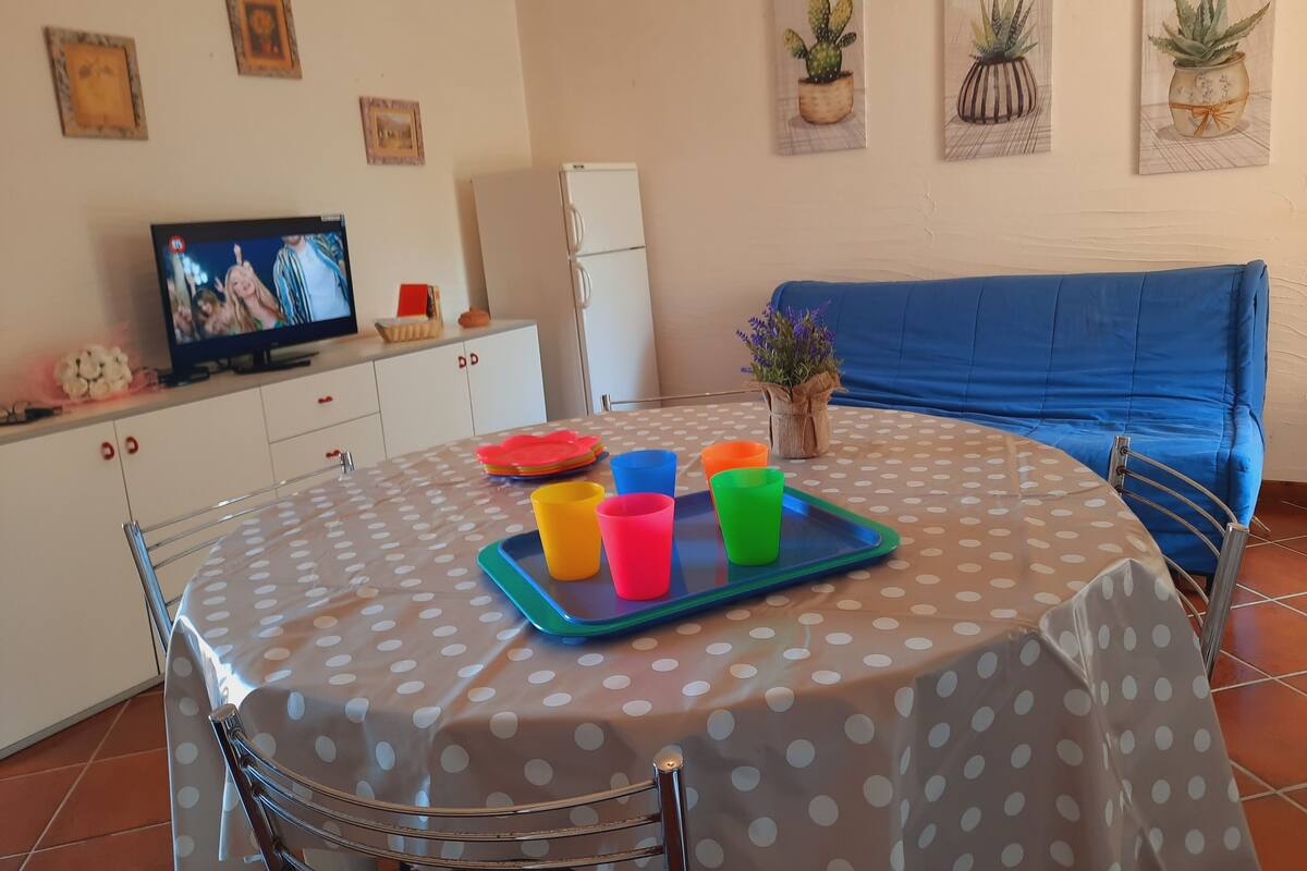 A dining area with a polka dot tablecloth, colorful cups, a TV, a refrigerator, and a blue sofa.