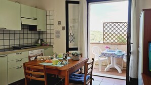 Eine Küche mit Essbereich, einem Tisch mit Vase und Gemälde, und Blick auf einen Garten durch eine Tür.