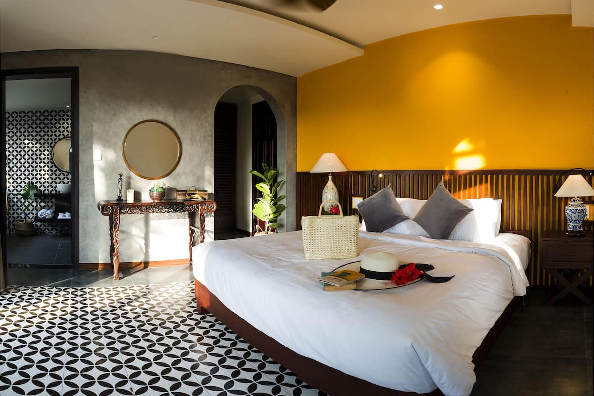 A hotel room with a large bed, a ceiling fan, a bedside table with a lamp, and a wall-mounted TV.