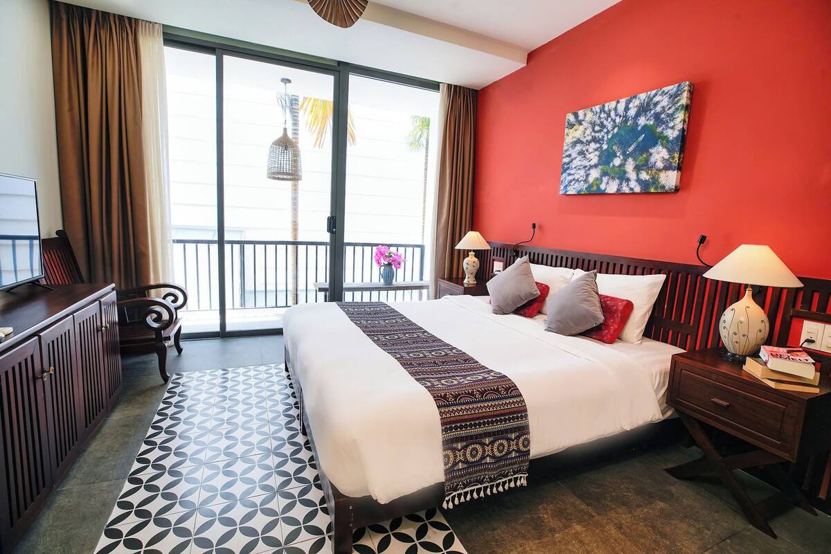 A hotel room with a large bed, a desk, a chair, a nightstand, and a view of the outdoors through a sliding door.