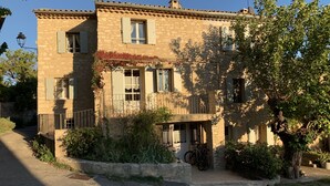 A two-story stone building with a balcony, a bicycle, and a tree in the foreground. - House with Provencal charm for lovers of authenticity. (Saignon)