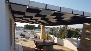 Une terrasse extérieure avec une table et des chaises, une pergola au-dessus et une vue sur le paysage urbain.