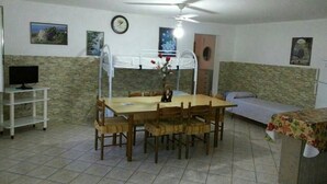 Une pièce comprenant une table à manger, des chaises, un lit superposé, un téléviseur et une horloge murale.