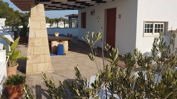 Un espace extérieur moderne, aménagé en terrasse, avec une pergola, un pilier en pierre et des plantes en pot.