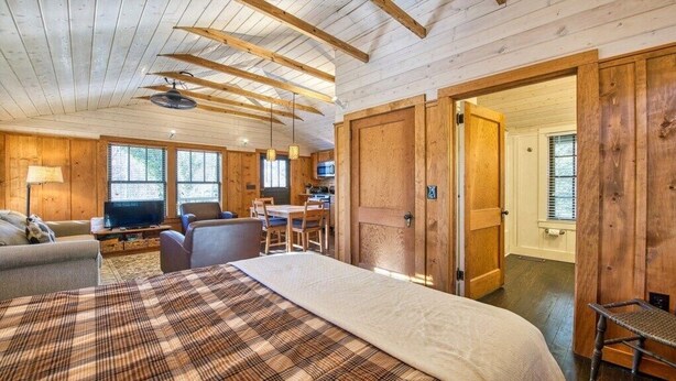Interior de una cabaña de madera con cama, sofá, mesa de comedor y sillas.