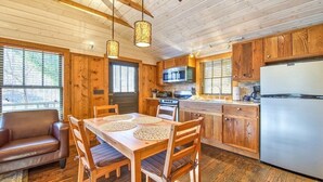 Interior de una cabaña de madera con una mesa de comedor, sillas, un sofá, una cocina con armarios de madera, un refrigerador y un microondas.