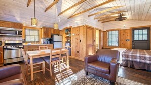 Interior de una cabaña de troncos con cocina, comedor y un solo dormitorio.
