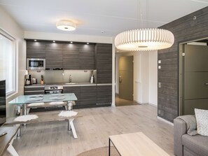 Een moderne keuken met donkere houten kastjes, roestvrijstalen apparatuur en een glazen eettafel met witte veren kussens.