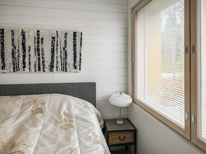 Een slaapkamer met een bed, een wanddecoratie in abstractie, een bedlamp en een raam met zonwering.