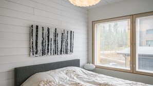 A bedroom with a bed, a window with blinds, and a wall-mounted abstract art piece.