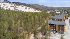 A lodge with a modern design, surrounded by a forested area and a snowy hillside.