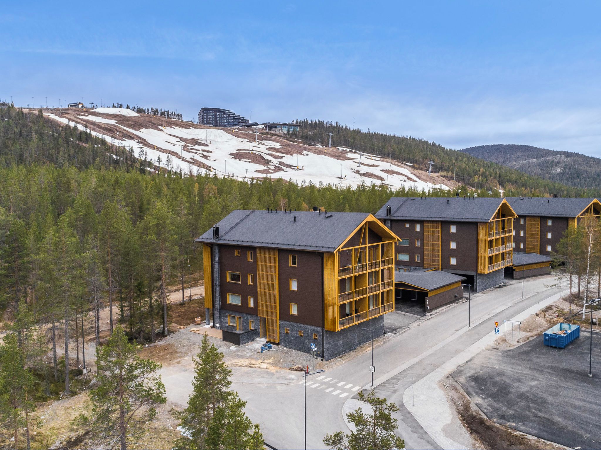 A modern building complex with multiple rooms, a parking area, and a snow-covered hill in the background.