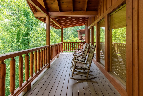 A wooden deck with a railing, a rocking chair, and a view of a forested area.