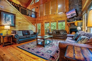 A spacious living room with a fireplace, wooden floors, and a large window overlooking greenery.