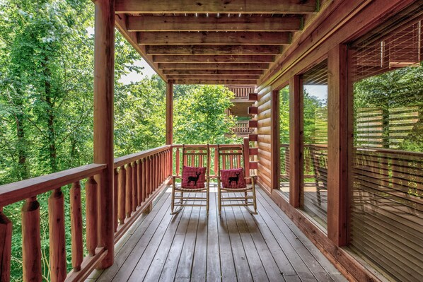 A wooden deck with two rocking chairs and a wooden railing. - Summer weeks reduced! Gated Resort, 6 Master Suites, Community Pool, Hot Tub! (Pigeon Forge)