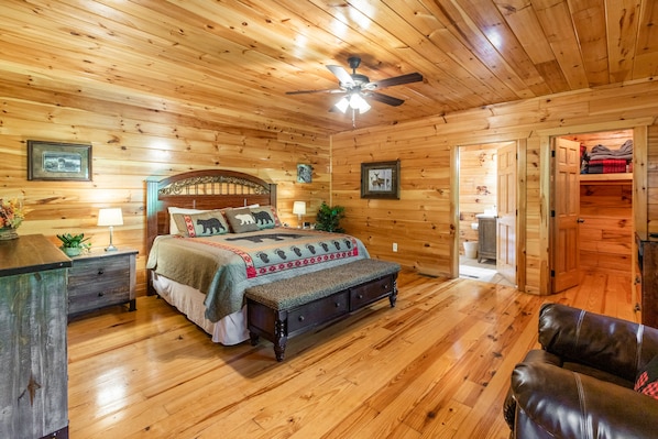 Un dormitorio con paneles de madera, una cama, mesitas de noche, un ventilador de techo y un vestidor.