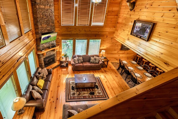 A cozy cabin interior with a fireplace, wooden walls, a sofa, a dining table, and a television.