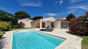 Ein Swimmingpool mit klarem, blauem Wasser, umgeben von einer Terrasse mit Liegestühlen und einem Sonnenschirm.