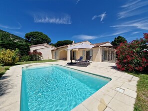 A swimming pool with a clear blue water, surrounded by a patio area with lounge chairs and an umbrella.