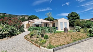 Ein Wohnhaus mit befestigter Auffahrt, einer überdachten Terrasse und einem Garten mit verschiedenen Pflanzen und Blumen.