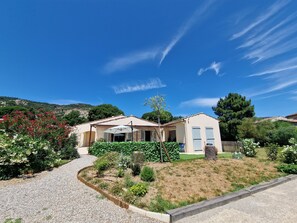 A residential property with a paved driveway, a covered patio, and a garden with various plants and flowers.