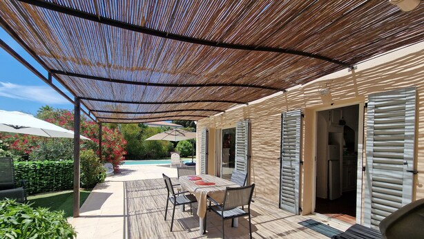 Ein überdachter Patio-Bereich mit Pool, Gartenmöbeln und Blick auf den Pool.