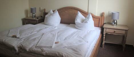 Una cama bien hecha con sábanas y almohadas blancas, dos mesitas de noche con lámparas y un cabecero de madera.