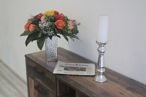 Una mesa de madera con un periódico, un florero de flores y una vela.