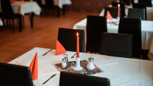 A restaurant setting with tables set for dining, featuring white tablecloths, red napkins, and candles. - Milde Hotel (Kalbe)