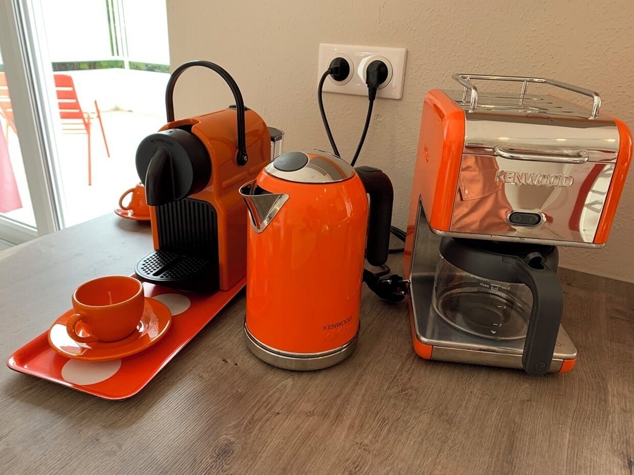 A kitchen area with a coffee maker, kettle, and a tray with a cup and saucer.