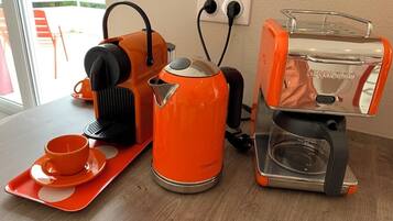 A kitchen area with a coffee maker, kettle, and a tray with a cup and saucer.