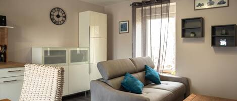 A modern living room with a sofa, a wooden coffee table, a wicker chair, a cabinet, a clock, and a window with curtains.