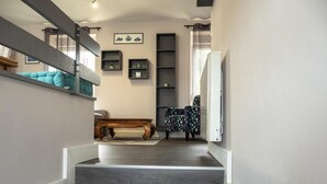 Un escalier menant à un espace de vie comprenant un canapé, un fauteuil à motifs et des étagères intégrées.