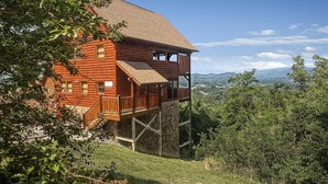 Eine Holzhütte mit Steinfundament, einer Holzterrasse und Blick auf die Berge.