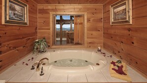Eine Holzdiele mit einer großen Badewanne, gerahmten Bildern an den Wänden und Blick auf eine verschneite Landschaft durch eine offene Tür.