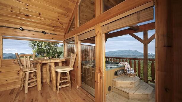 Eine Holzterrasse mit Whirlpool, Holzstühlen und einem Tisch mit Gläsern und einer Flasche.