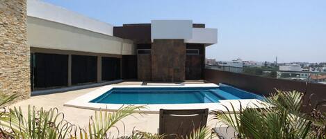 Una piscina en la azotea con un muro de piedra y vistas a la ciudad.