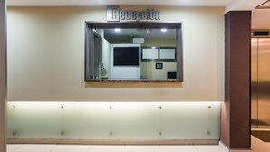 Zona de recepción con un separador de vidrio, mostrador de recepción y señalización en la pared.