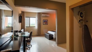 Una habitación de hotel moderna con un escritorio de vidrio, un sofá cómodo, una mesita pequeña y una silla de masajes.