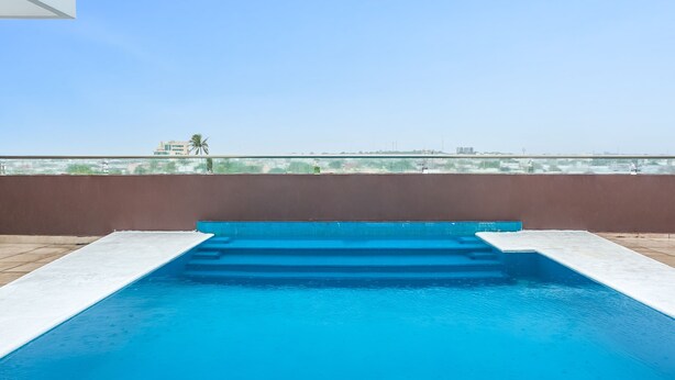Una piscina en la azotea con agua azul cristalina, rodeada por un muro marrón y una barandilla de vidrio.
