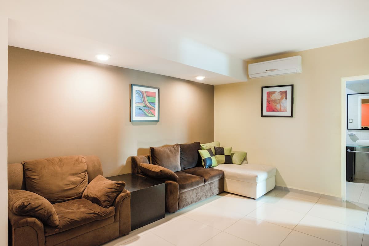 Uma sala de estar moderna com um sofá seccional marrom, um banquinho branco e duas pinturas abstratas emolduradas nas paredes.