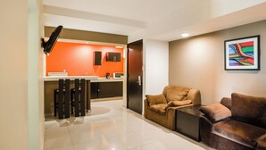Una sala de estar moderna con un sofá marrón, una mesa de centro y una zona de cocina con una pared de acento naranja.